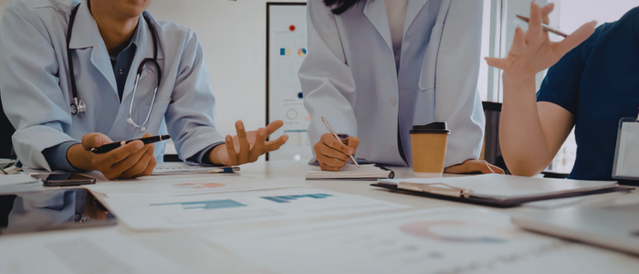 Healthcare professionals discuss data and review documents around a table during a clinical research or regulatory meeting.